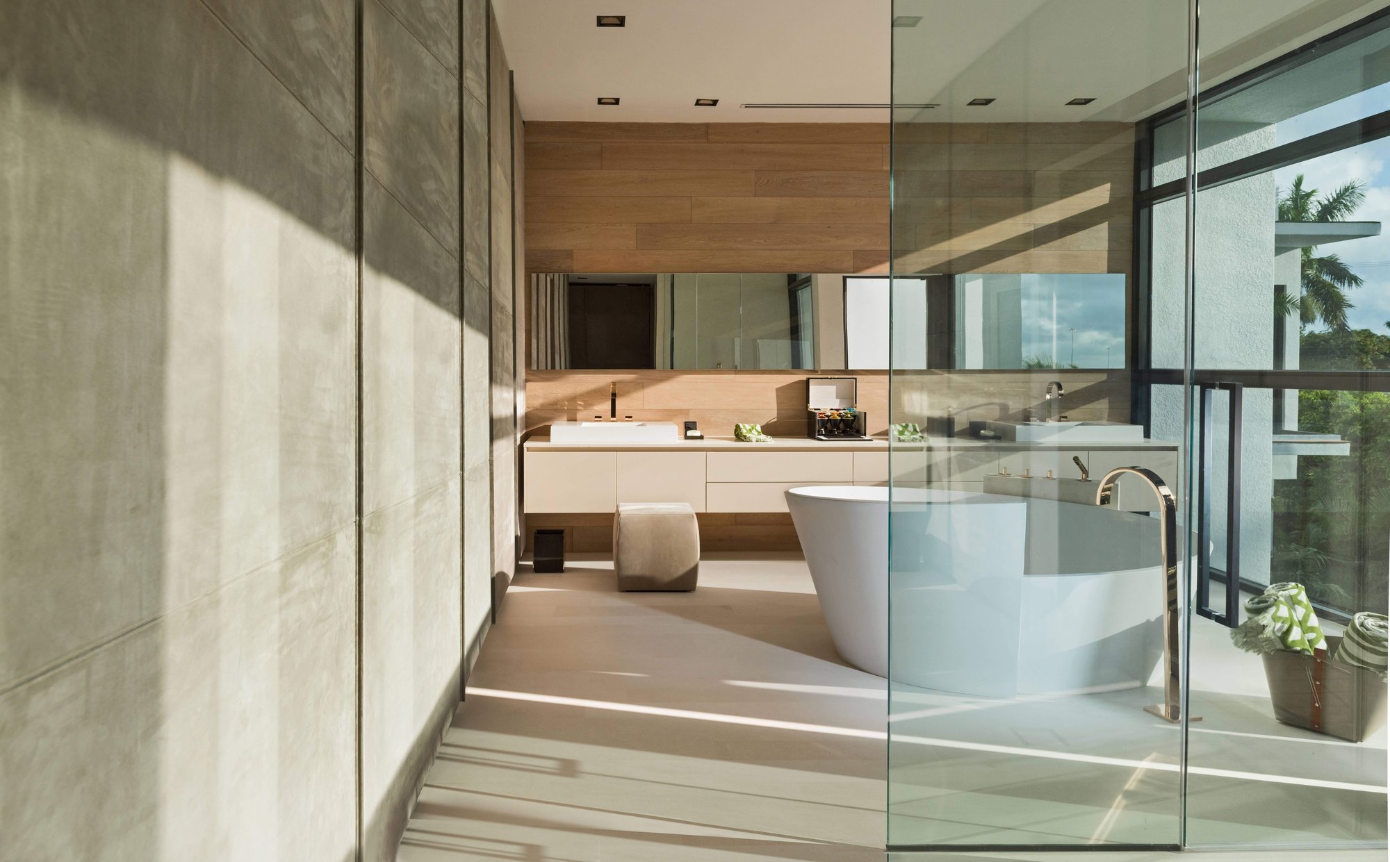 Modernist luxury bathroom with floor-to-ceiling textured gray concrete wall panels, natural wood accent walls and custom cabinetry, a freestanding bathtub.