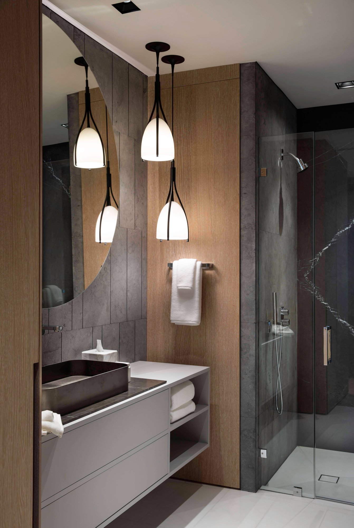 Floating grey bathroom vanity with a black stone vessel sink, marble countertop, and integrated wood wall paneling.