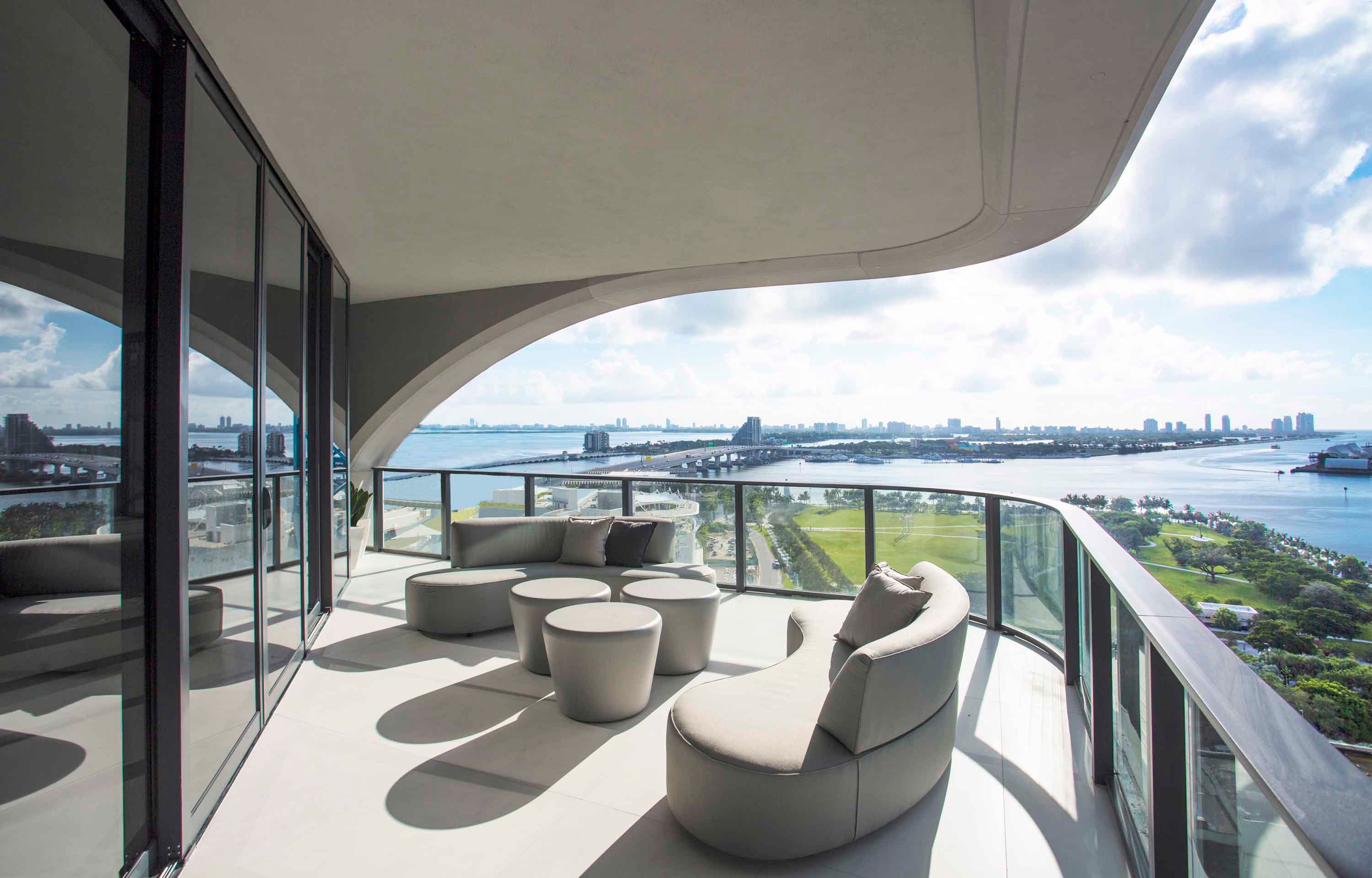Architectural balcony at One Thousand Museum featuring curved concrete overhangs, grey outdoor sofas, and a scenic bay view. Photo by Robin Hill.
