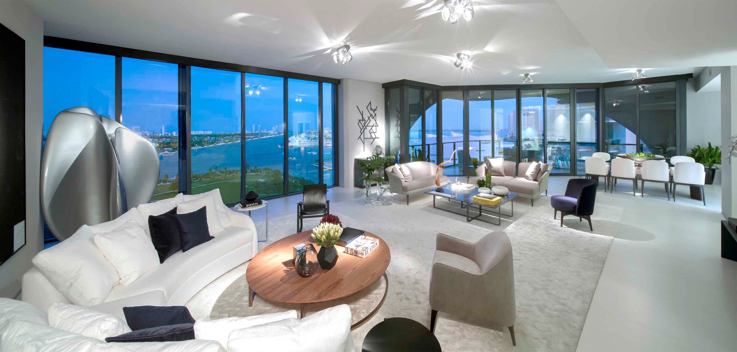 Luxury open-concept living room at One Thousand Museum with custom curved sofas, a walnut coffee table, and panoramic floor-to-ceiling windows. Photo by Robin Hill.