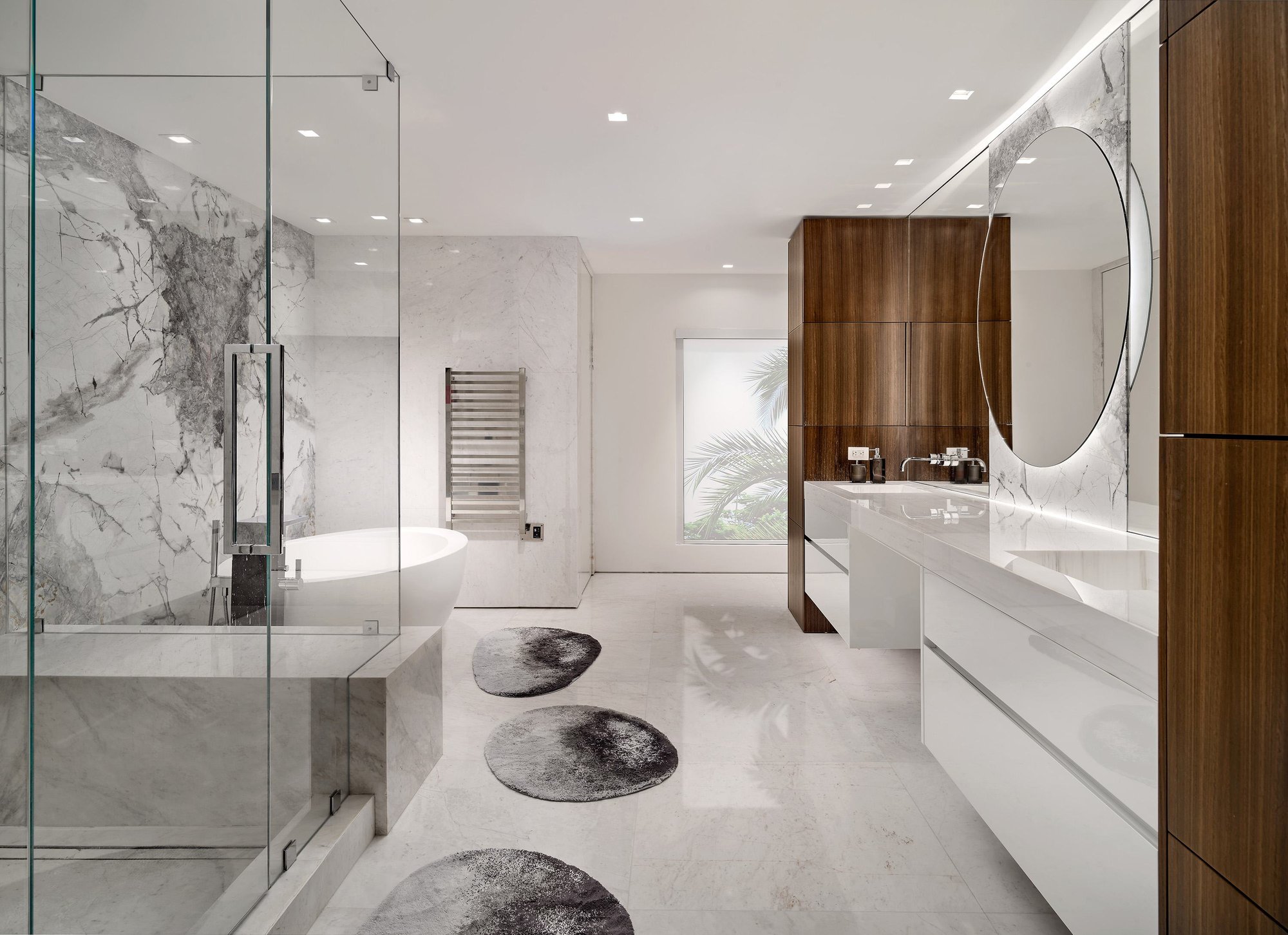 Contrast-driven luxury bathroom featuring textured gray marble walls and floors, a warm walnut wood panel wall, a floating dark wood vanity with white sinks, and a freestanding soaking tub.