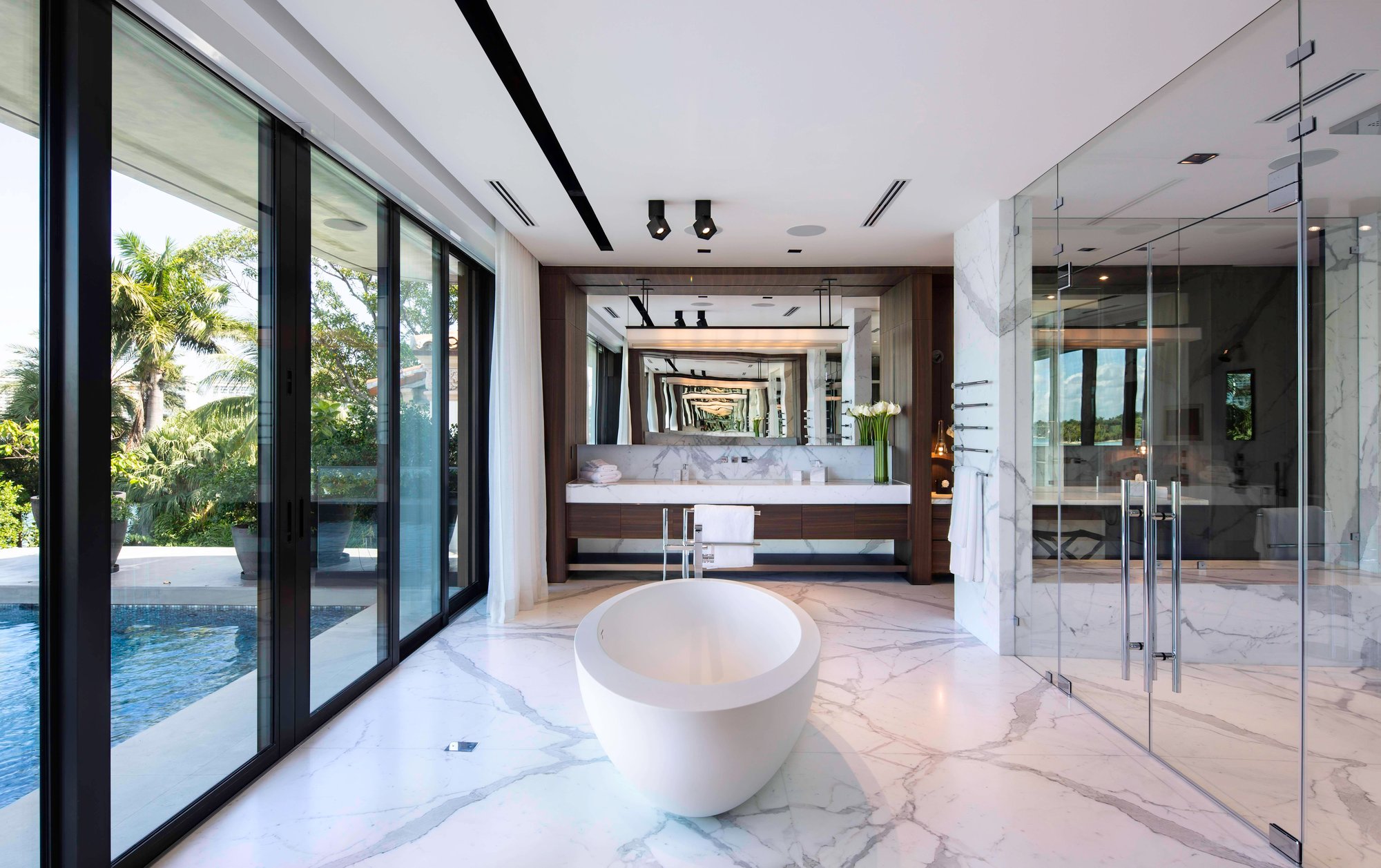 Modern master bath with white marble flooring, a freestanding oval soaking tub, and a custom dark wood floating vanity.