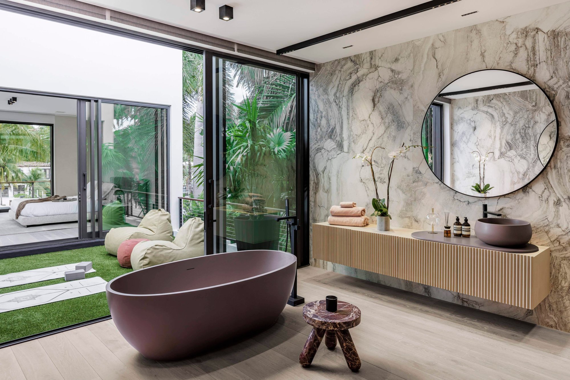 Avant-garde luxury bathroom featuring bookmatched gray marble walls, a fluted light wood floating vanity with a dark gray vessel sink, and a statement matte mauve freestanding tub.
