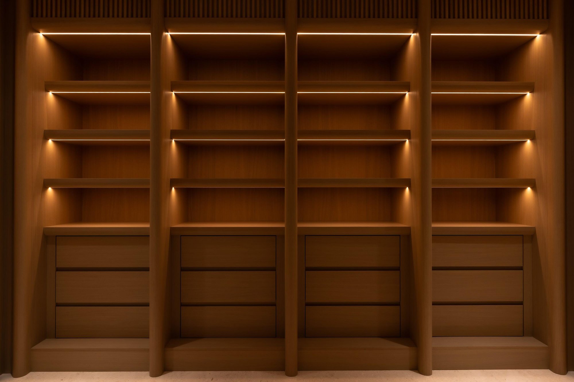 Custom wood closet with rounded vertical pillars, open shelving, and warm LED accent lighting.