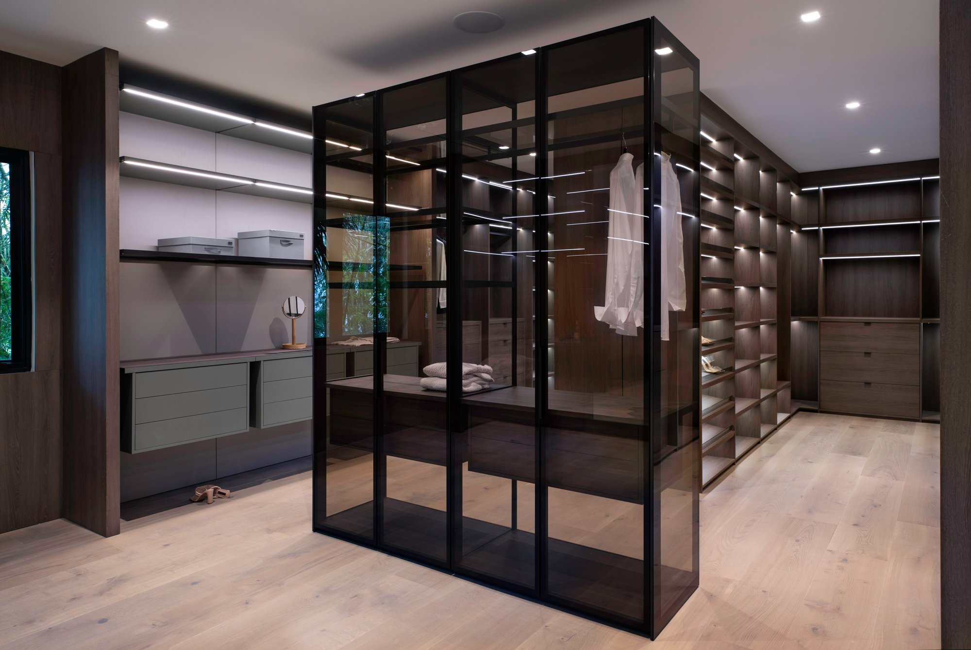 Luxury walk-in closet featuring a smoked glass display island and dark wood perimeter shelving with LED lighting.
