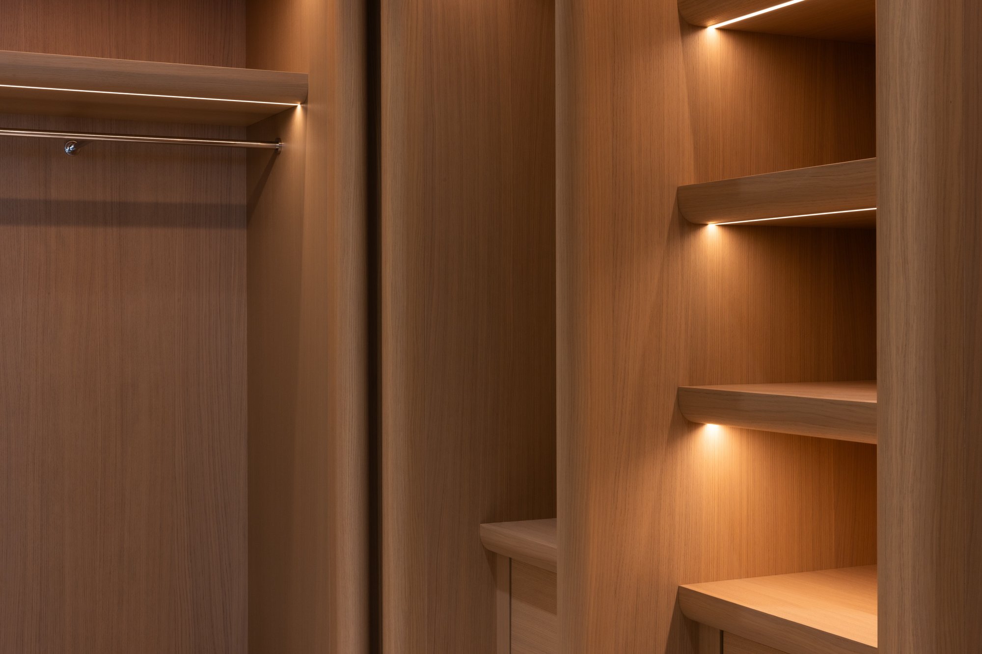 Warm wood custom closet with curved dividers and integrated LED shelf lighting.