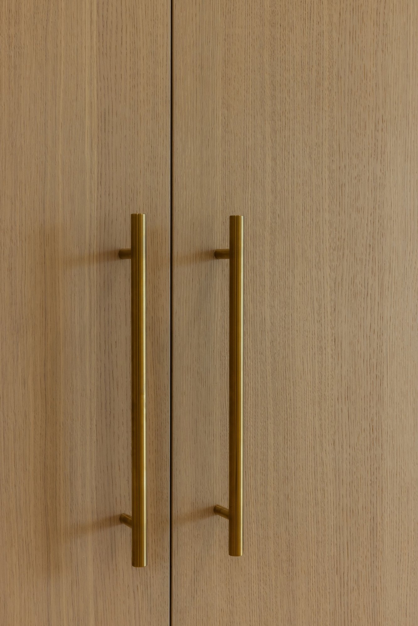 Close-up of light oak wood cabinetry with vertical brushed gold bar handles.