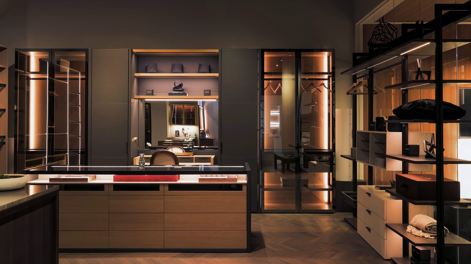 Luxury walk-in closet with integrated vanity, illuminated glass doors, and a wood island dresser.