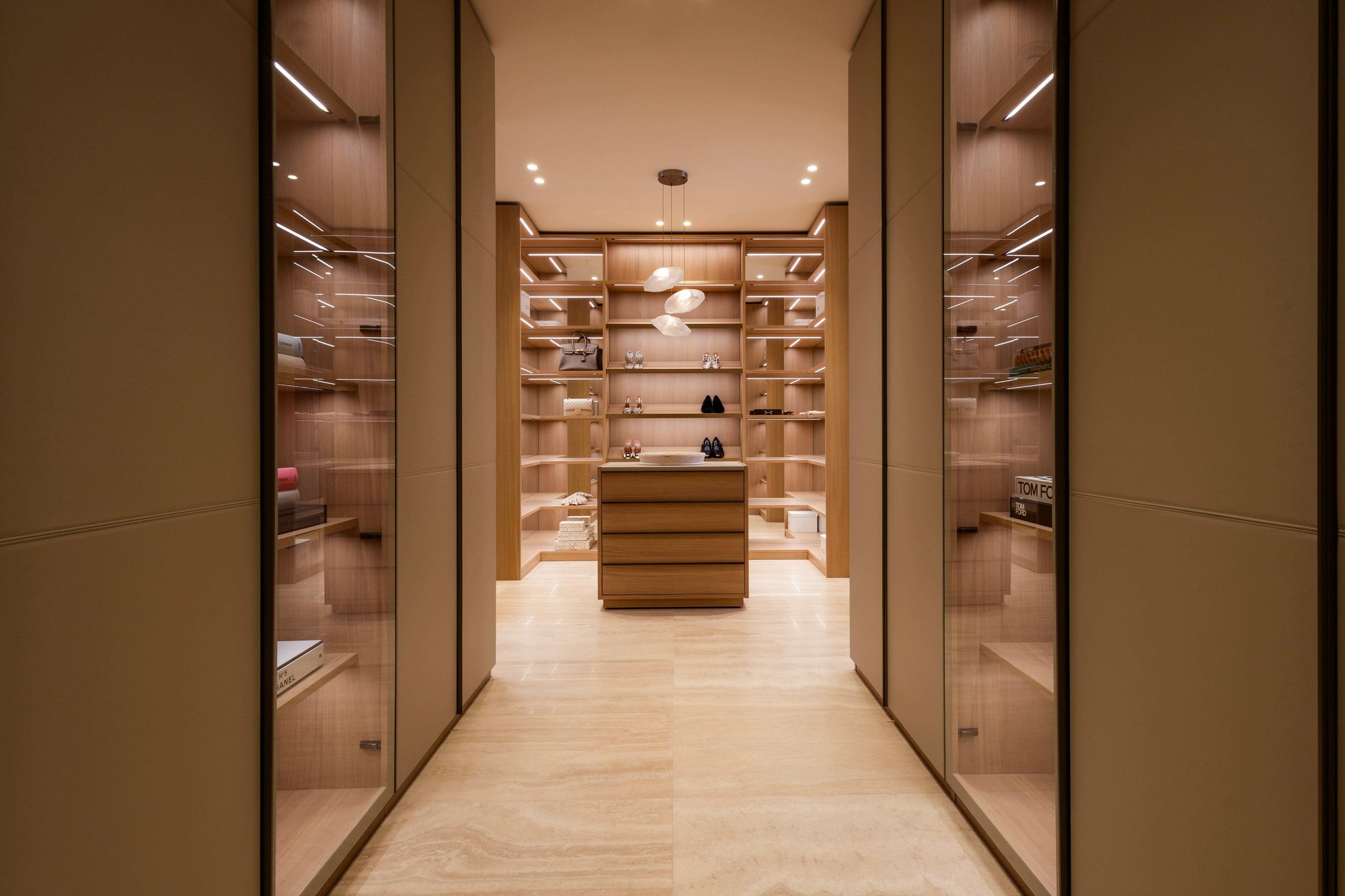 Luxury walk-in closet featuring floor-to-ceiling custom natural wood cabinetry with integrated shelf lighting, and a central dresser island under an organic pendant light.